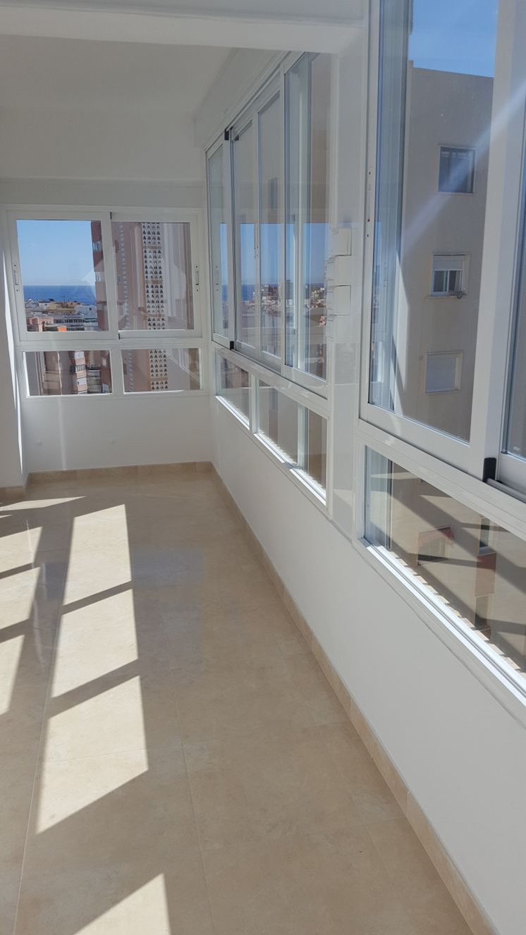 A narrow enclosed glazed balcony with a bright tiled floor